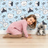 Lovely child standing in front of Whimsy Tots Woodland Scribble Friends Wallpaper in Blue with bear, bunny, fox, raccoon, flower, leaf in design. Lovely child standing in front of Whimsy Tots Woodland Scribble Friends Wallpaper in Blue with bear, bunny, fox, raccoon, flower, leaf in design.