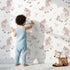 Lovely child standing in front of Whimsy Tots Feathered DaydreamโฏUnicorn Wallpaper in White with unicorn, feather, moon, star, leaf in design. Lovely child standing in front of Whimsy Tots Feathered DaydreamโฏUnicorn Wallpaper in White with unicorn, feather, moon, star, leaf in design.