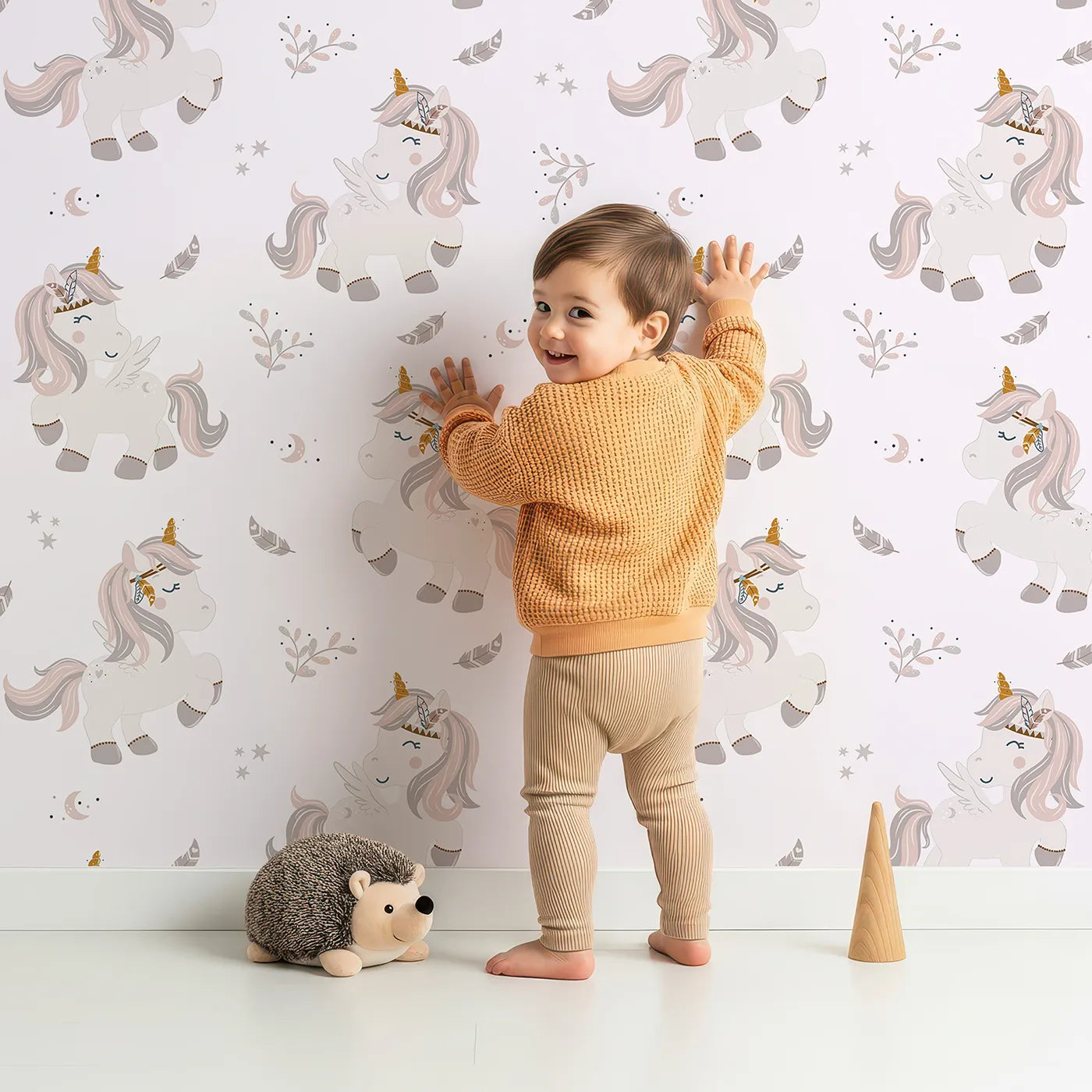 Lovely child standing in front of Whimsy Tots Feathered Daydreamβ―Unicorn Wallpaper in BlushΒ Pink with unicorn, feather, moon, star, leaf in design.