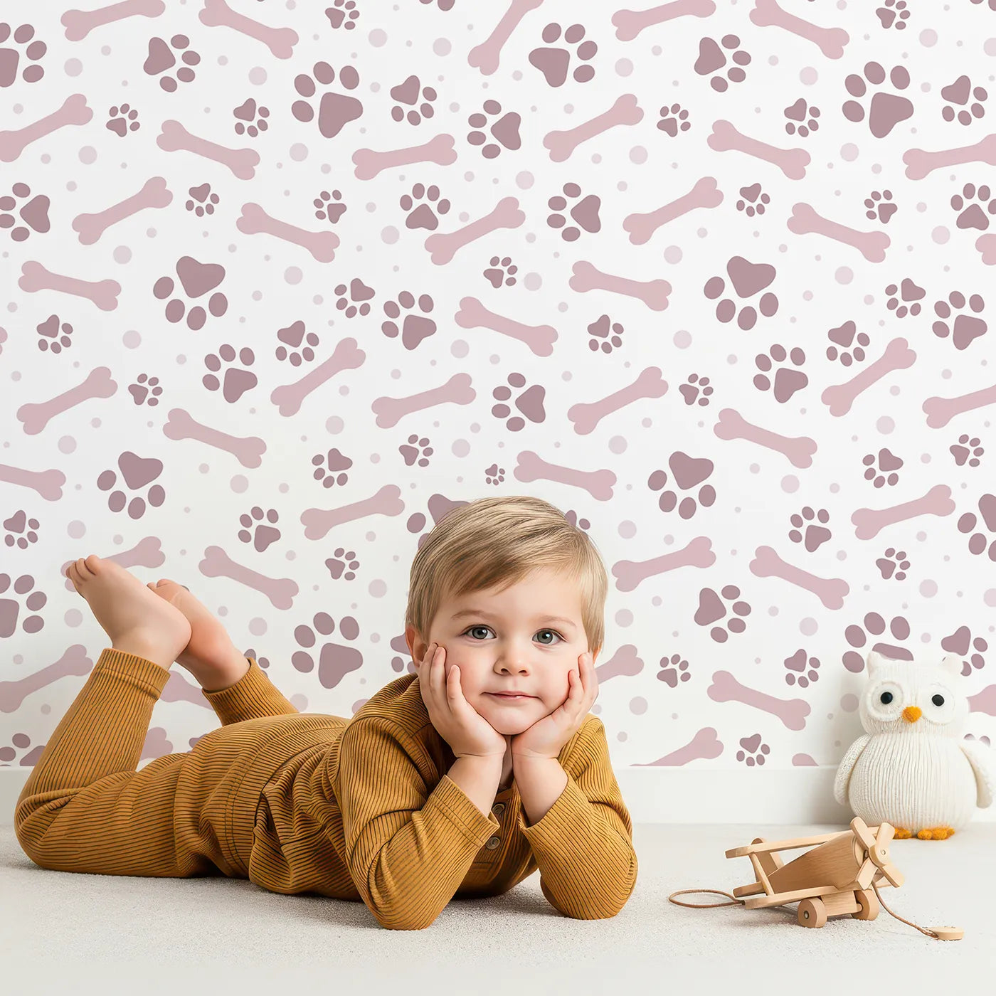 Lovely child standing in front of Whimsy Tots Puppy Paw Parade Wallpaper in Blush Pink with paw, bone, dot in design.