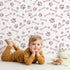 Lovely child standing in front of Whimsy Tots Puppy Paw Parade Wallpaper in Blush Pink with paw, bone, dot in design. Lovely child standing in front of Whimsy Tots Puppy Paw Parade Wallpaper in Blush Pink with paw, bone, dot in design.