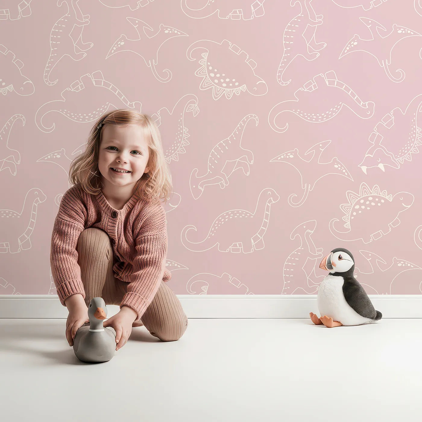 Lovely child standing in front of Whimsy Tots Dino Scribble Parade Wallpaper in Blush Pink with dinosaur, stegosaurus, triceratops, pterosaur in design.