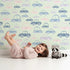 Lovely child standing in front of Whimsy Tots Tiny Toot Toot Cars Wallpaper in Sage Green with car, vehicle, pastel, transportation in design. Lovely child standing in front of Whimsy Tots Tiny Toot Toot Cars Wallpaper in Sage Green with car, vehicle, pastel, transportation in design.