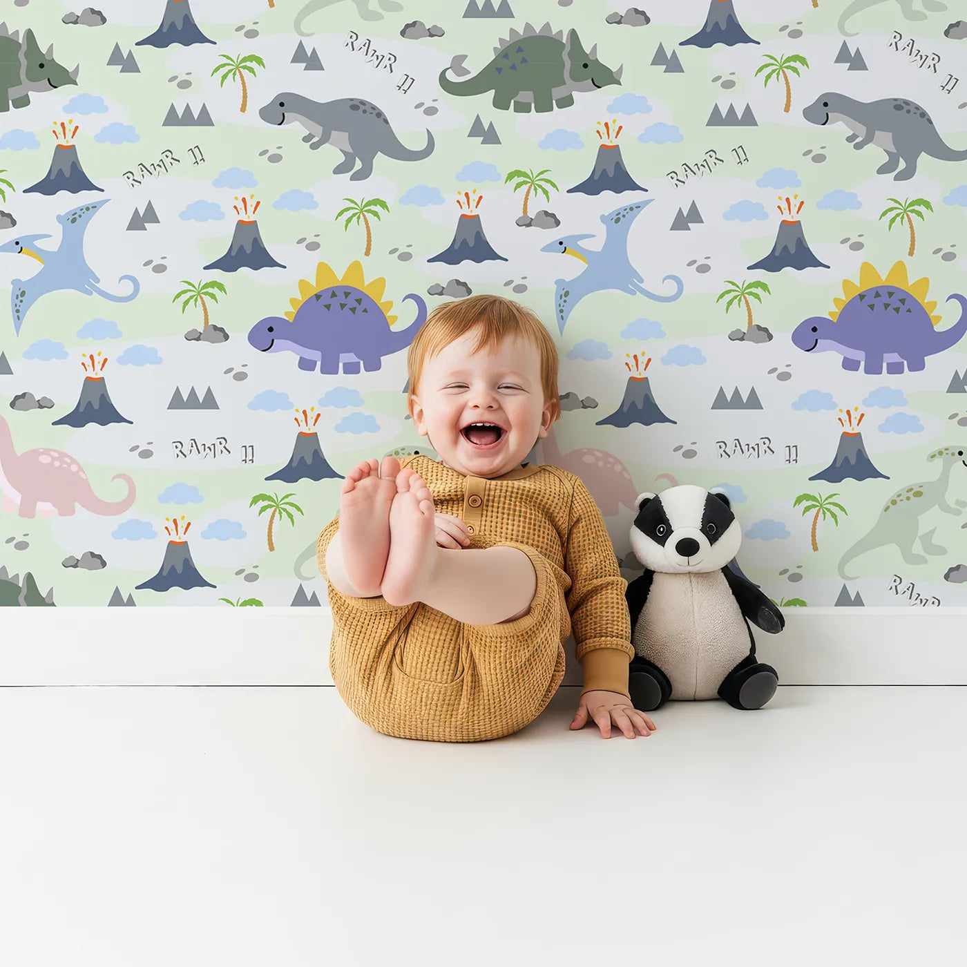 Lovely child standing in front of Whimsy Tots Rawr-some Dino Land Wallpaper in Mint Green with dinosaur, volcano, palm tree, mountain, cloud in design.