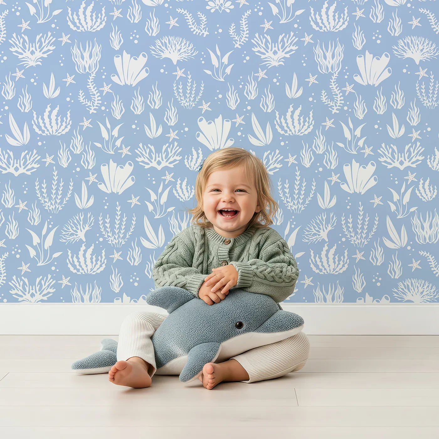 Lovely child standing in front of Whimsy Tots Coral Garden Dance Wallpaper in Ocean Blue with coral, seaweed, starfish, bubble in design.