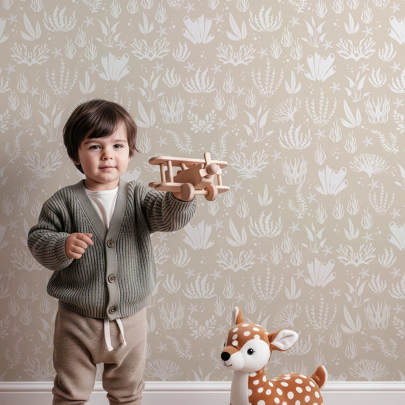 Lovely child standing in front of Whimsy Tots Coral Garden Dance Wallpaper in Sand Beige with coral, seaweed, starfish, bubble in design.