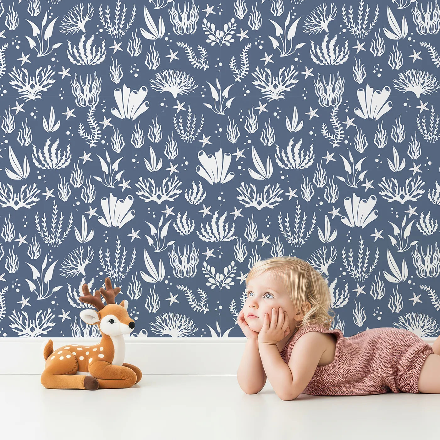 Lovely child standing in front of Whimsy Tots Coral Garden Dance Wallpaper in Deep Indigo with coral, seaweed, starfish, bubble in design.
