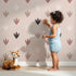 Lovely child standing in front of Whimsy Tots Dino Tracks Wallpaper in Rose Clay Brown with footprint, dinosaur, track, print in design. Lovely child standing in front of Whimsy Tots Dino Tracks Wallpaper in Rose Clay Brown with footprint, dinosaur, track, print in design.