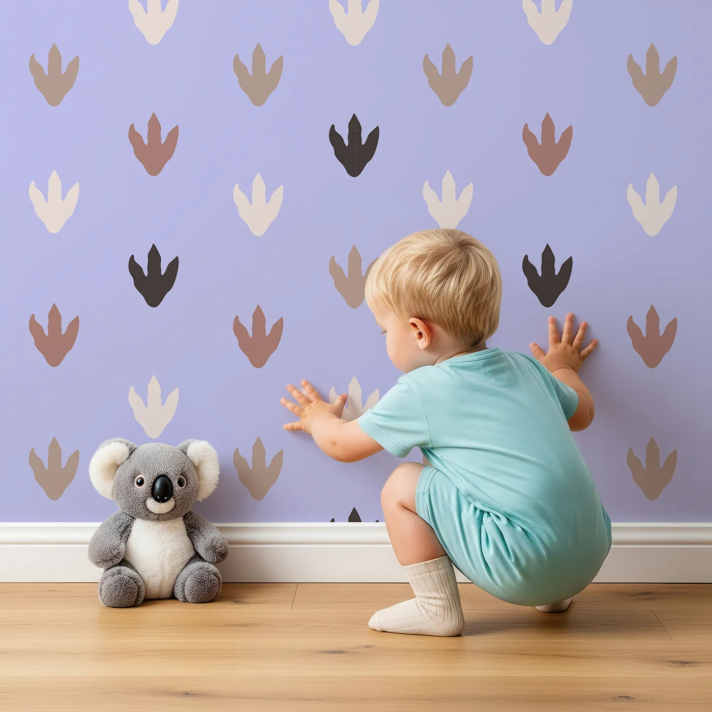 Lovely child standing in front of Whimsy Tots Dino Tracks Wallpaper in Lavender Gray with footprint, dinosaur, track, print in design.