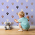 Lovely child standing in front of Whimsy Tots Dino Tracks Wallpaper in Lavender Gray with footprint, dinosaur, track, print in design. Lovely child standing in front of Whimsy Tots Dino Tracks Wallpaper in Lavender Gray with footprint, dinosaur, track, print in design.
