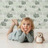 Lovely child standing in front of Whimsy Tots Monstera Jungle Wallpaper in Mint Mist Green with leaf, monstera, jungle, foliage in design. Lovely child standing in front of Whimsy Tots Monstera Jungle Wallpaper in Mint Mist Green with leaf, monstera, jungle, foliage in design.