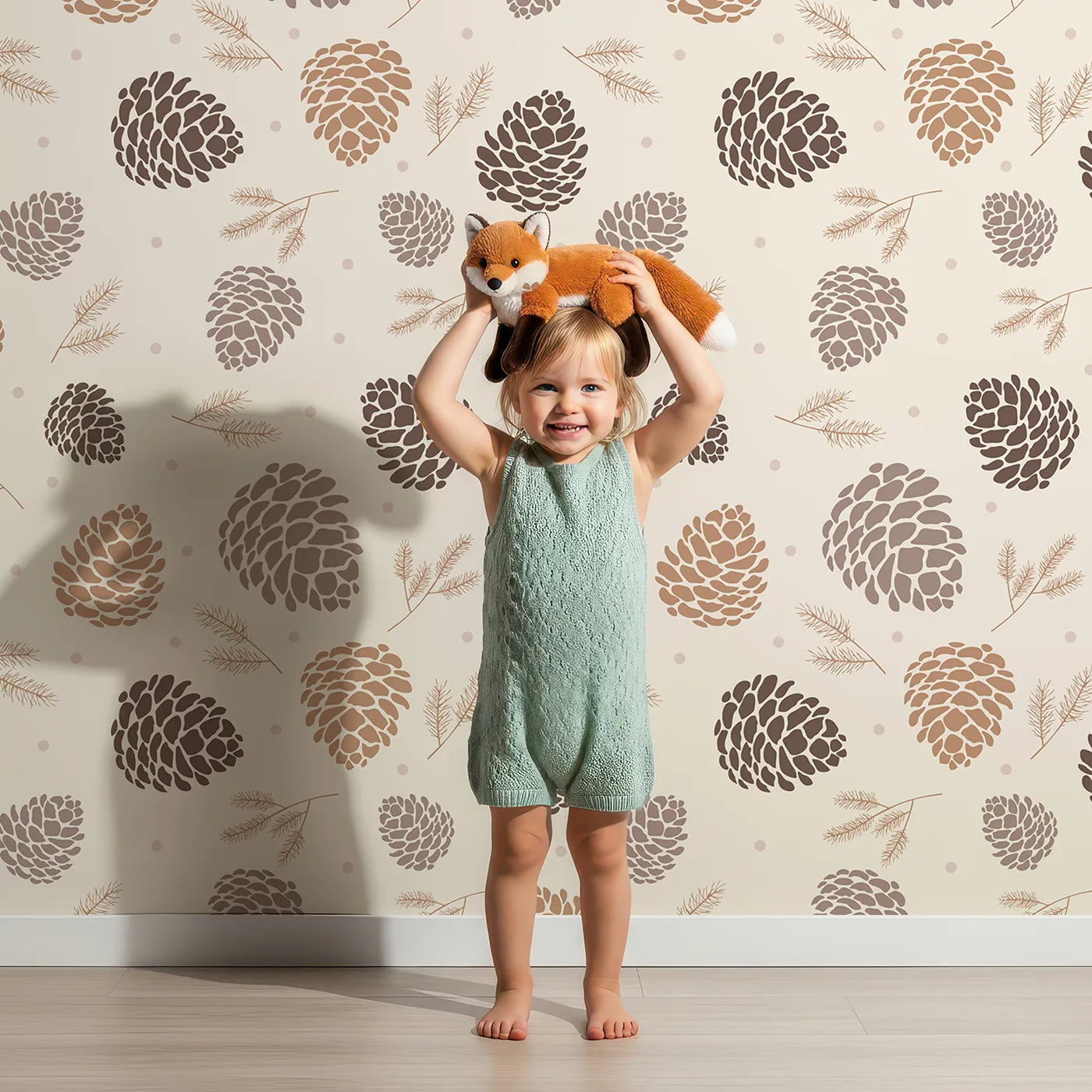 Lovely child standing in front of Whimsy Tots Pinecone Whispers Wallpaper in Cozy Taupe with pinecone, needle, forest, woodland in design.