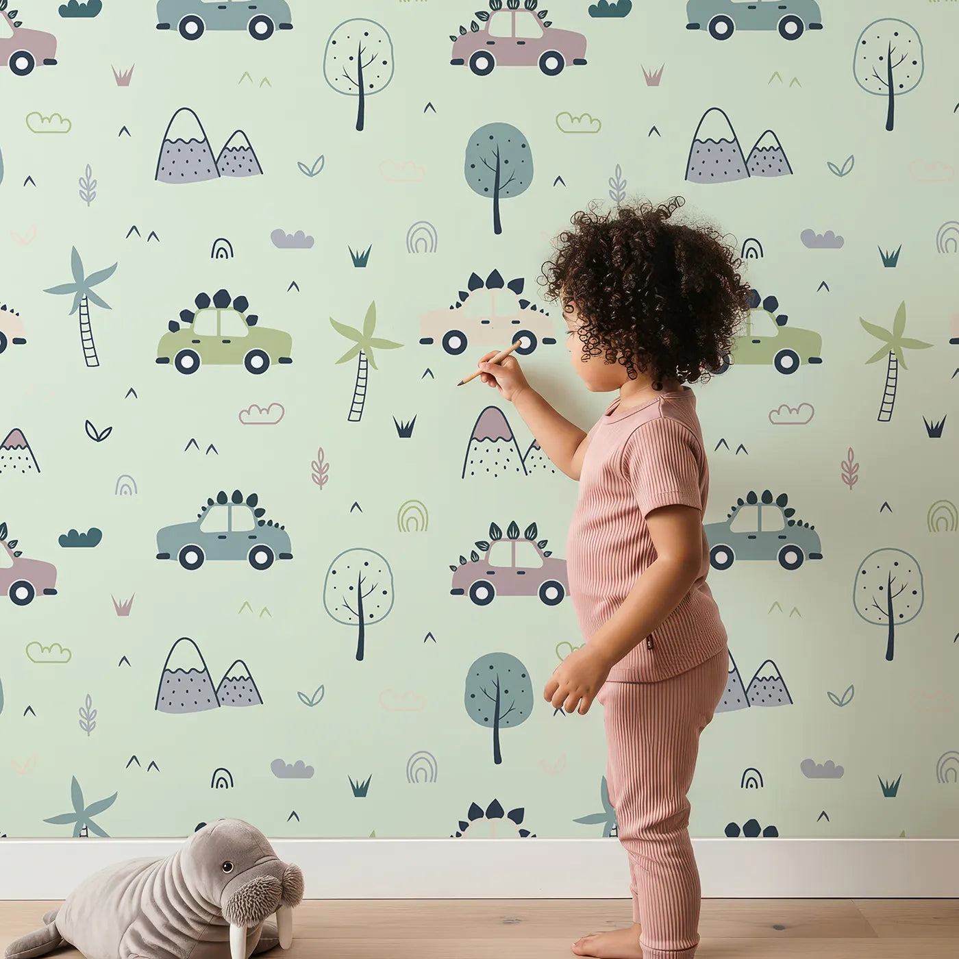 Lovely child standing in front of Whimsy Tots Dino Drivers Parade Wallpaper in Mint Green with dinosaur, car, tree, rainbow, mountain in design.