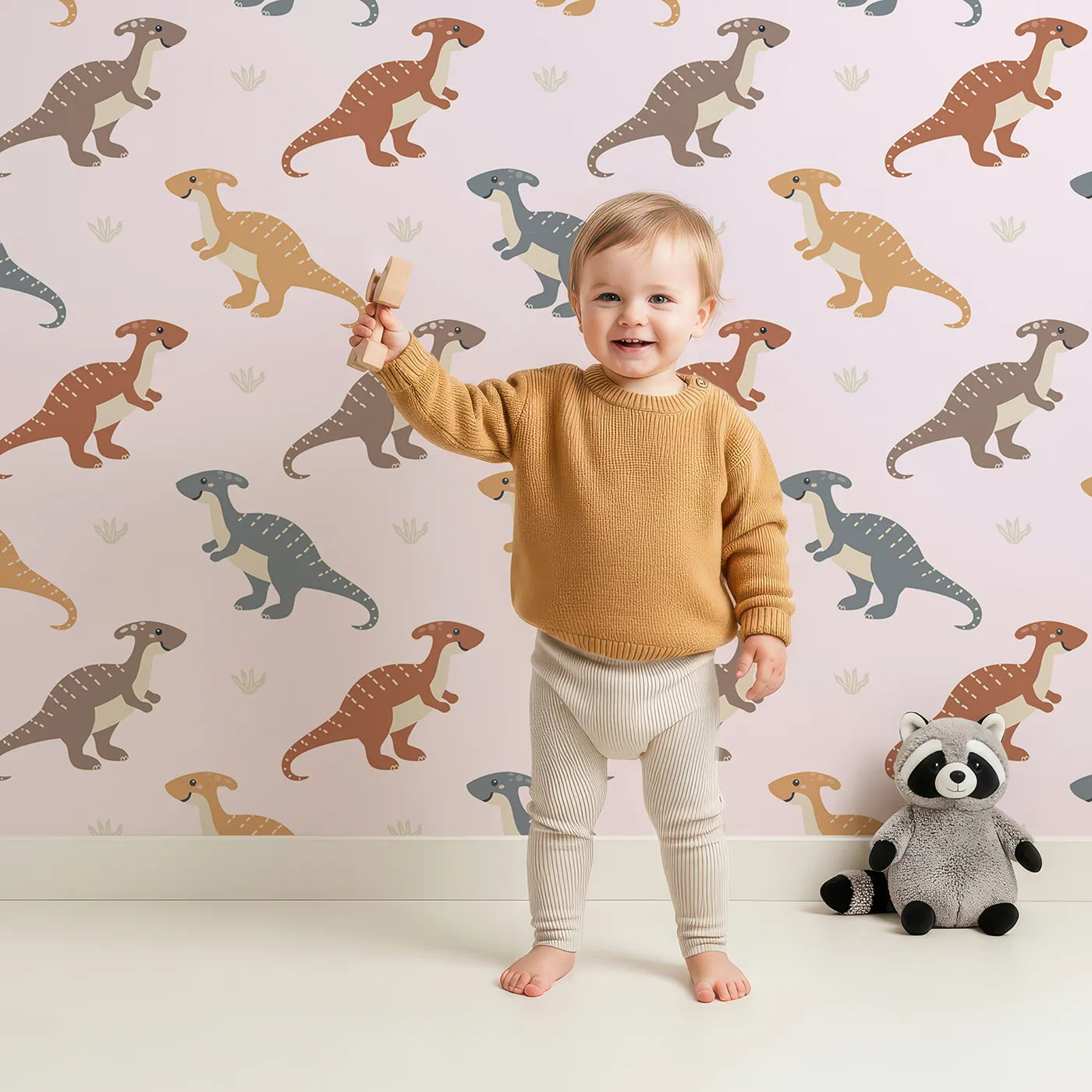 Lovely child standing in front of Whimsy Tots Gentle Dino Trek Wallpaper in Blush Pink with dinosaur, footprint, plant in design.