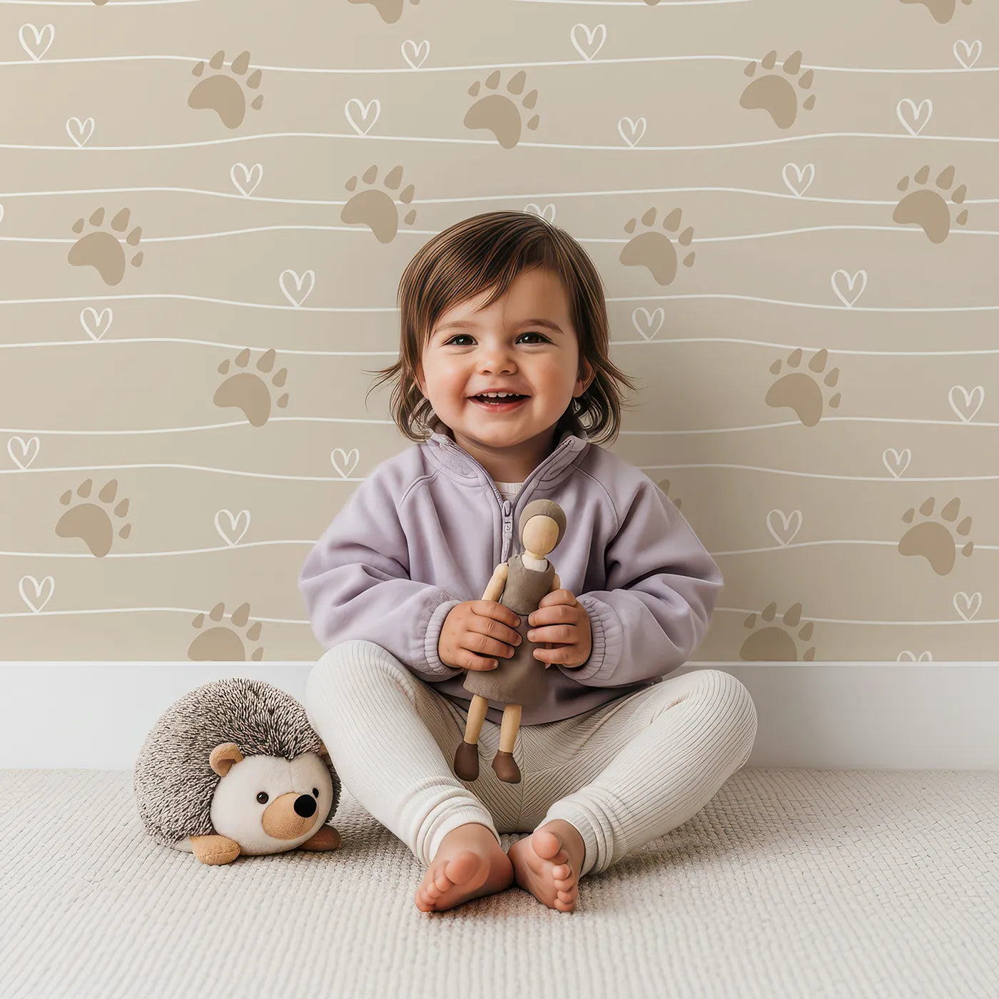 Lovely child standing in front of Whimsy Tots Bear Hug Trail Wallpaper in Oat Beige with bear, paw print, heart, line in design.