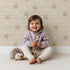 Lovely child standing in front of Whimsy Tots Bear Hug Trail Wallpaper in Oat Beige with bear, paw print, heart, line in design. Lovely child standing in front of Whimsy Tots Bear Hug Trail Wallpaper in Oat Beige with bear, paw print, heart, line in design.