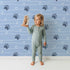 Lovely child standing in front of Whimsy Tots Bear Hug Trail Wallpaper in Sky Blue with bear, paw print, heart, line in design. Lovely child standing in front of Whimsy Tots Bear Hug Trail Wallpaper in Sky Blue with bear, paw print, heart, line in design.