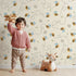 Lovely child standing in front of Whimsy Tots Busy Bee Trail Wallpaper in Buttercream with bee, flower, leaf, heart, trail in design. Lovely child standing in front of Whimsy Tots Busy Bee Trail Wallpaper in Buttercream with bee, flower, leaf, heart, trail in design.
