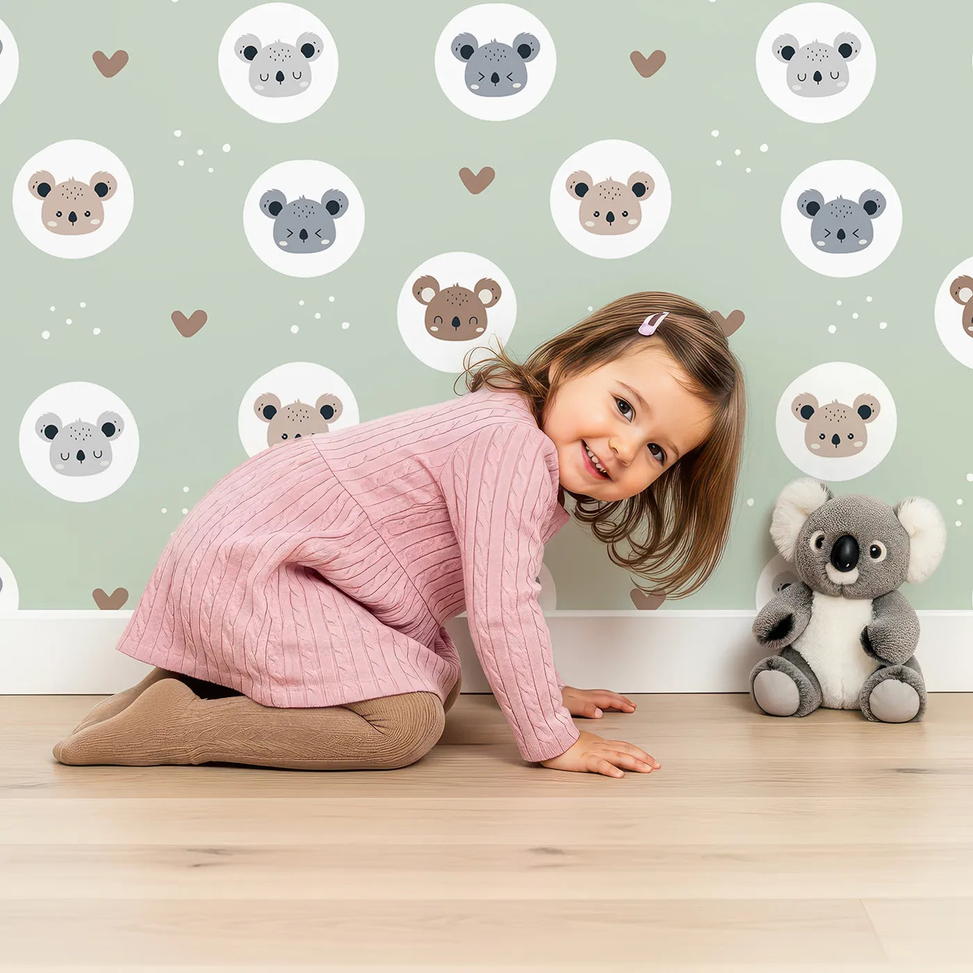 Lovely child standing in front of Whimsy Tots Cuddly Koala Circle Wallpaper in Sage Green with koala, heart, circle, dot, face in design.