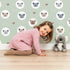 Lovely child standing in front of Whimsy Tots Cuddly Koala Circle Wallpaper in Sage Green with koala, heart, circle, dot, face in design. Lovely child standing in front of Whimsy Tots Cuddly Koala Circle Wallpaper in Sage Green with koala, heart, circle, dot, face in design.
