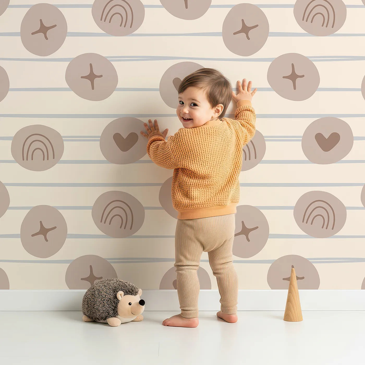 Lovely child standing in front of Whimsy Tots Boho Rhythm Doodle Wallpaper in Soft Beige with rainbow, heart, star, stripe, doodle in design.