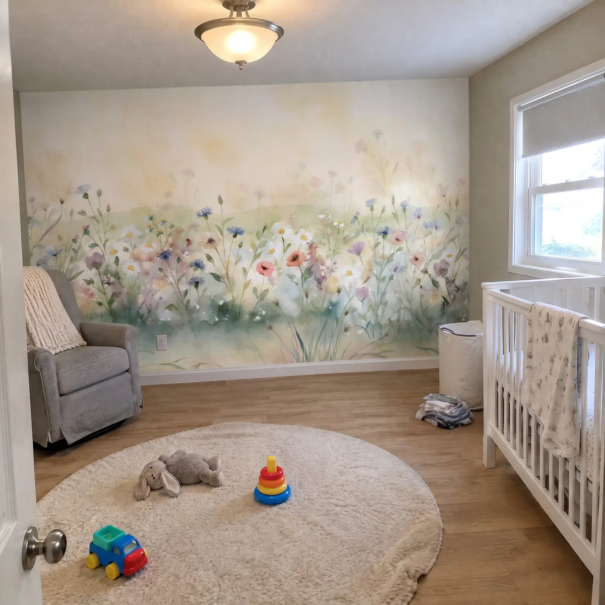 Nursery with a soft watercolor wildflower wallpaper mural, pastel blooms on a cream sky, beside a grey glider and white crib