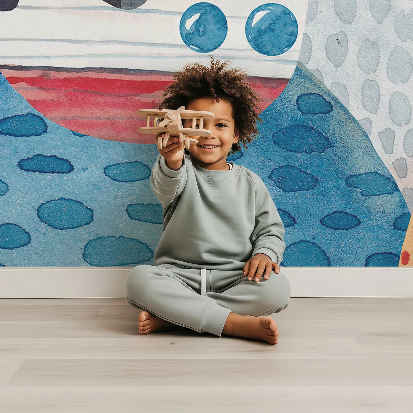 Child in front of Whimsy Tots Watercolor Mountain Voyage Wall Mural with boat, mountain, sea, sun, watercolor, landscape, bird, adventure in design.