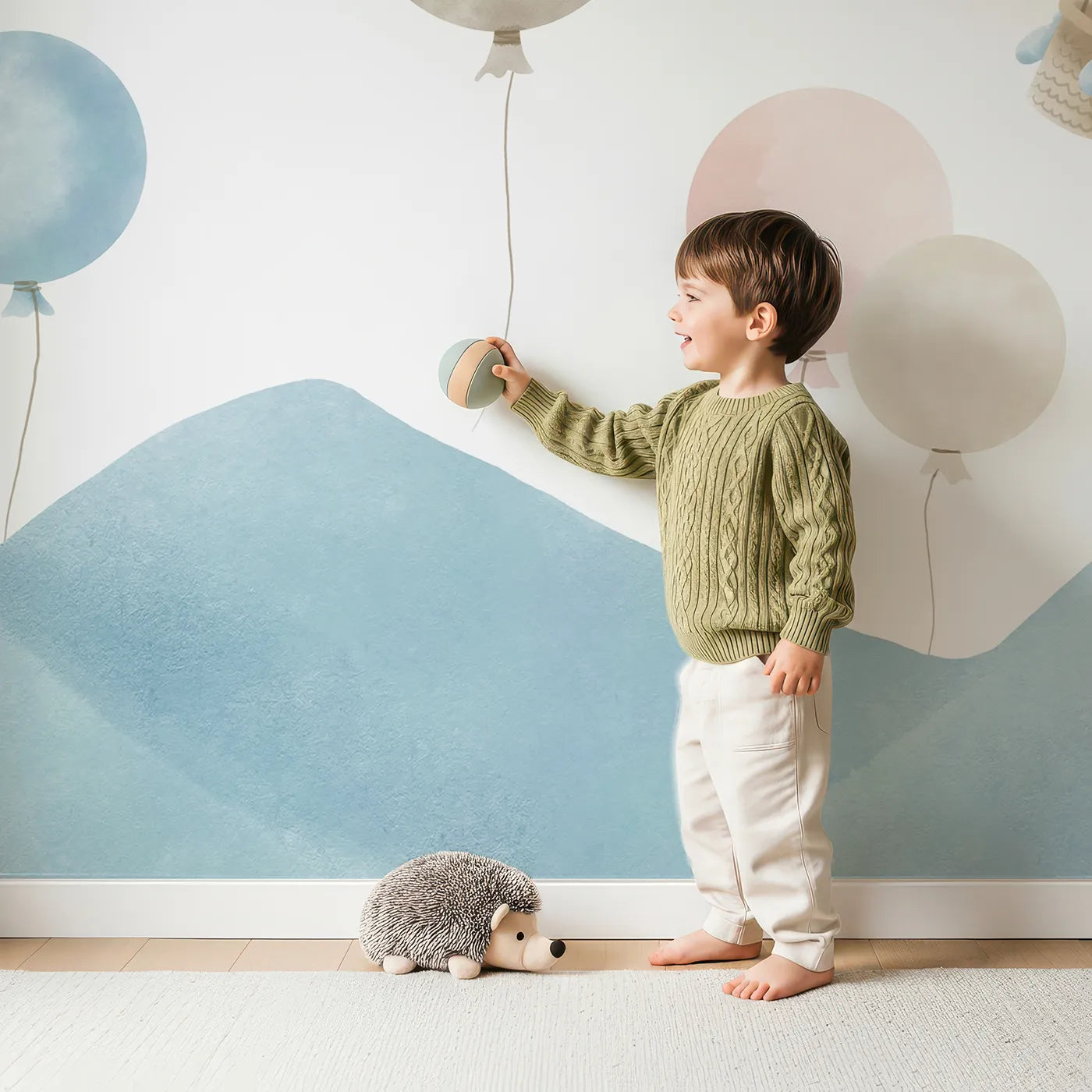 Child in front of Whimsy Tots Pastel Sky Balloon Parade Wall Mural with balloon, hot air balloon, sky, mountain, cloud, pastel, pink, blue in design.