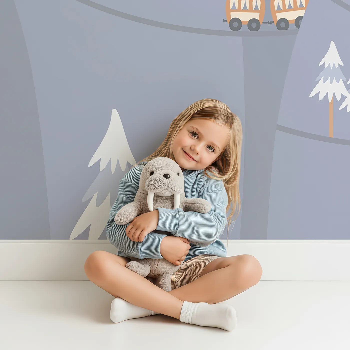 Child in front of Whimsy Tots Mountain Train Adventure Wall Mural in Blue with train, mountain, hill, house, hot air balloon, bridge, tree in design.