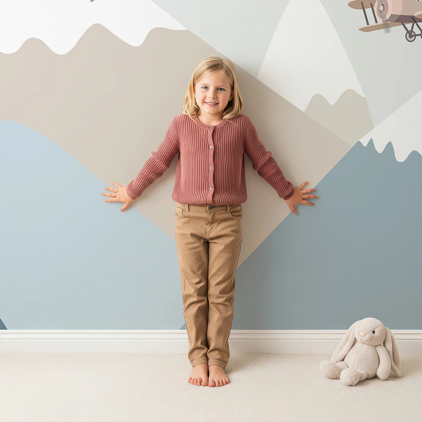 Child in front of Whimsy Tots Mountain Air Rally Wall Mural with airplane, balloon, mountain, vintage, modern, minimalist, blue, beige in design.
