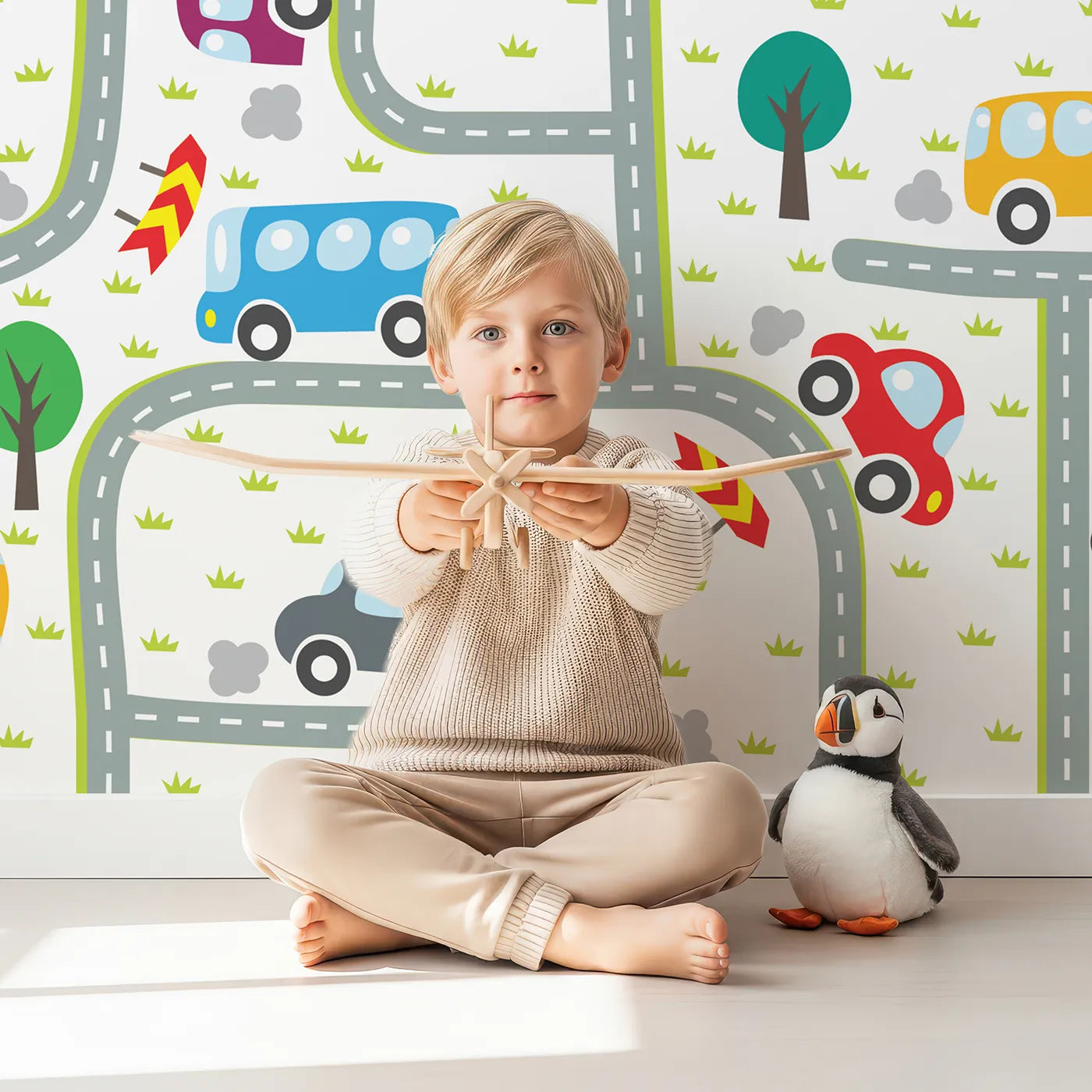 Child in front of Whimsy Tots Busy Roads Wall Mural with car, road, town, city, tree, truck, bus, rocket in design.