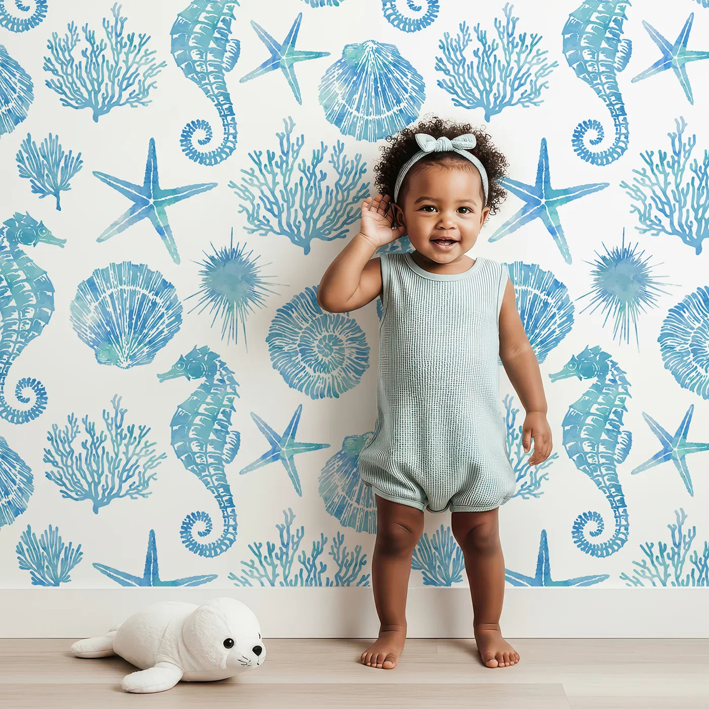 Lovely child standing in front of Whimsy Tots Watercolor Ocean Treasures Wallpaper in Blue with ocean, sea, seahorse, shell, starfish in design.