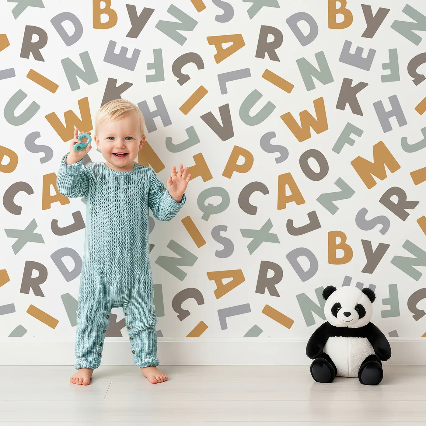 Lovely child standing in front of Whimsy Tots Earthy Alphabet Scatter Wallpaper with alphabet, letter, learning, neutral, earth tone in design.