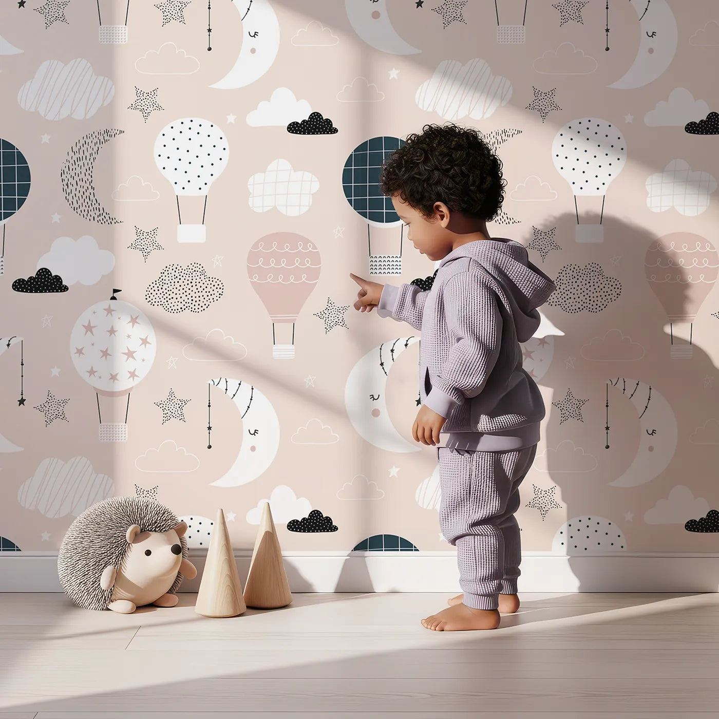 Lovely child standing in front of Whimsy Tots Boho Night Sky Wallpaper in Pink with moon, star, hot air balloon, cloud, boho in design.