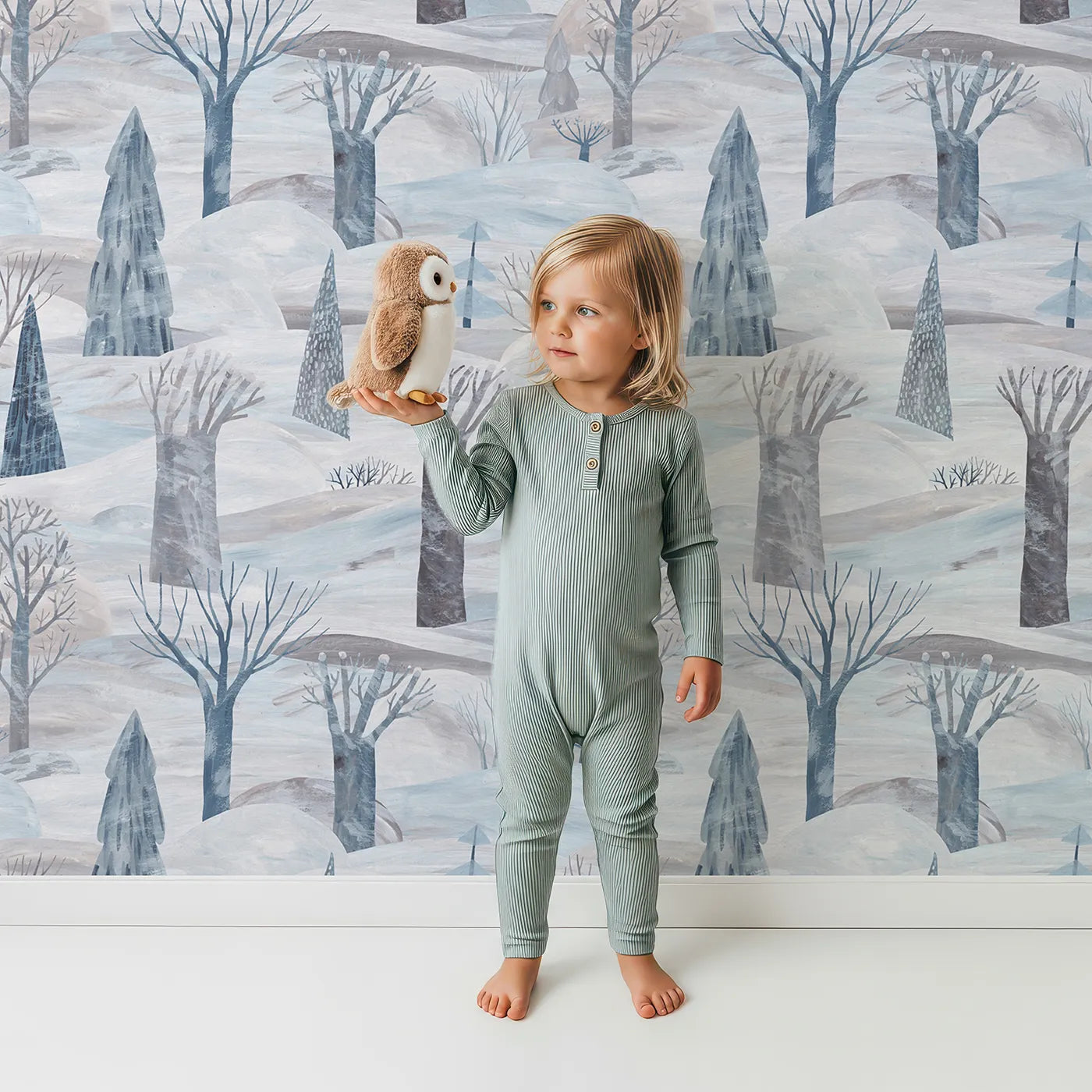 Lovely child standing in front of Whimsy Tots Painted Nordic Winter Wallpaper with winter, snow, tree, abstract, painted in design.