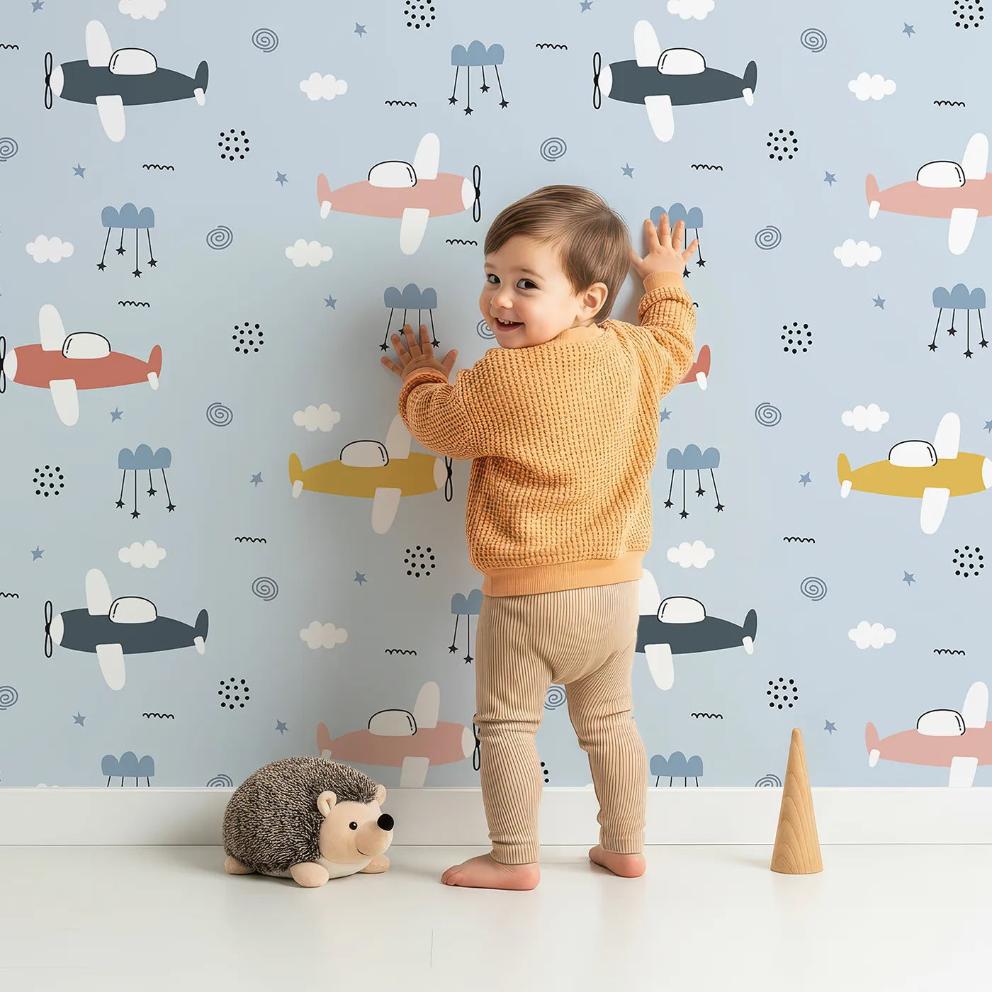 Lovely child standing in front of Whimsy Tots Colorful Propeller Planes Wallpaper with plane, airplane, sky, colorful, cartoon in design.