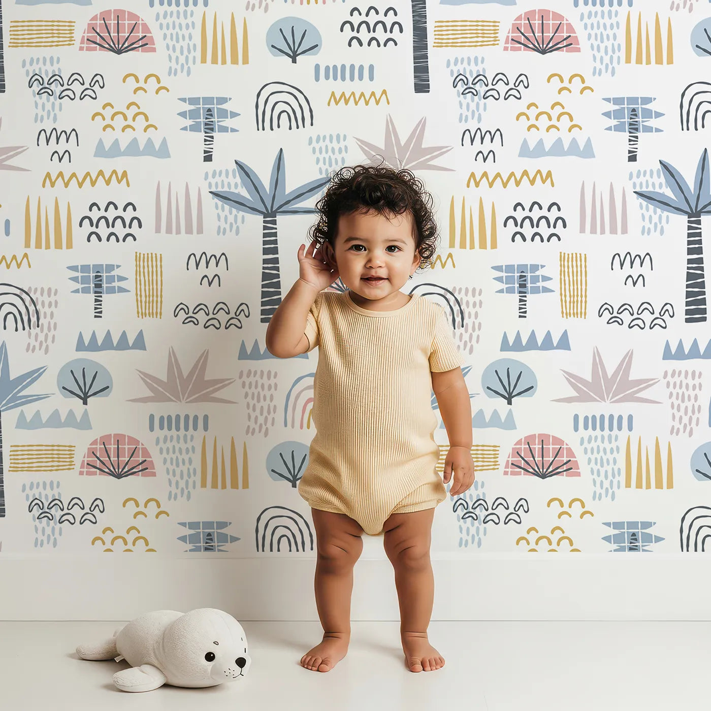 Lovely child standing in front of Whimsy Tots Abstract Tropical Shapes Wallpaper with abstract, tropical, palm tree, rainbow, boho in design.