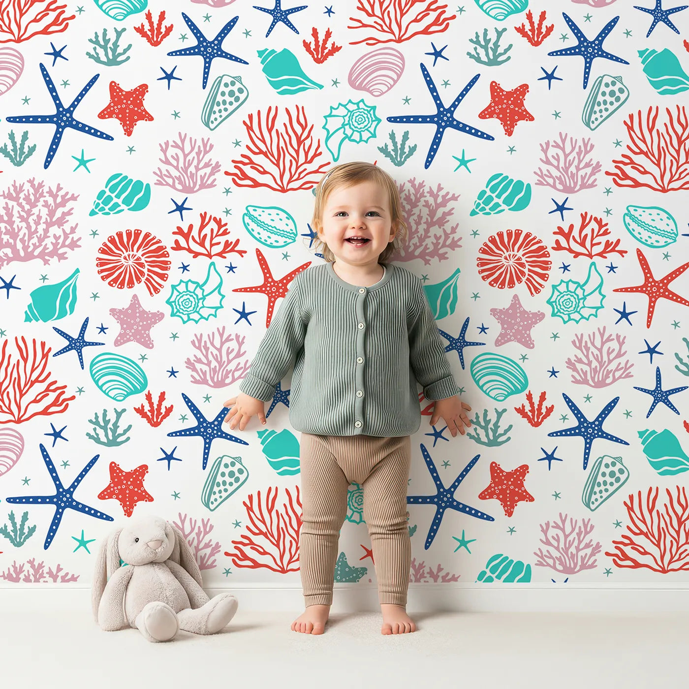 Lovely child standing in front of Whimsy Tots Vibrant Coral Reef Wallpaper with coral, starfish, shell, ocean, sea in design.