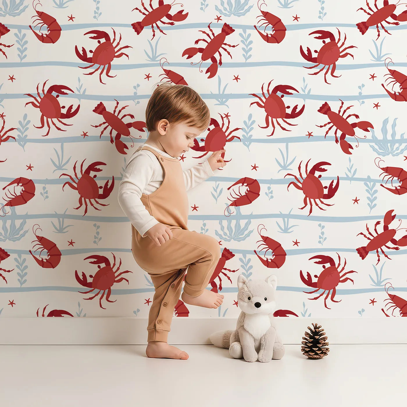 Lovely child standing in front of Whimsy Tots Red Crustacean Celebration Wallpaper with crab, lobster, shrimp, sea, stripe in design.