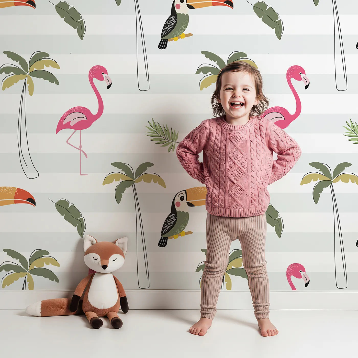 Lovely child standing in front of Whimsy Tots Striped Tropical Birds Wallpaper with toucan, flamingo, palm tree, tropical, stripe in design.