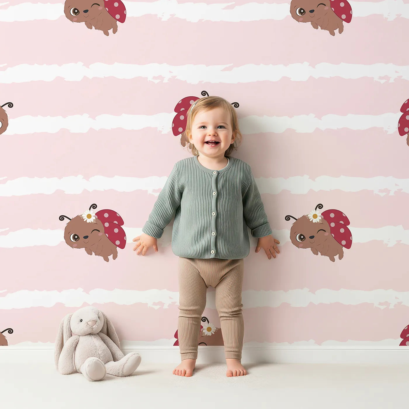 Lovely child standing in front of Whimsy Tots Winkie the Ladybug Wallpaper in Pink with ladybug, stripe, flower, bug in design.