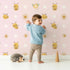 Lovely child standing in front of Whimsy Tots Buzzberry Bee Parade Wallpaper in Pink with bee, flower, daisy, dot in design.