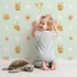 Lovely child standing in front of Whimsy Tots Buzzberry Bee Parade Wallpaper in Green with bee, flower, daisy, dot in design.