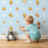 Lovely child standing in front of Whimsy Tots Buzzberry Bee Parade Wallpaper in Blue with bee, flower, daisy, dot in design.