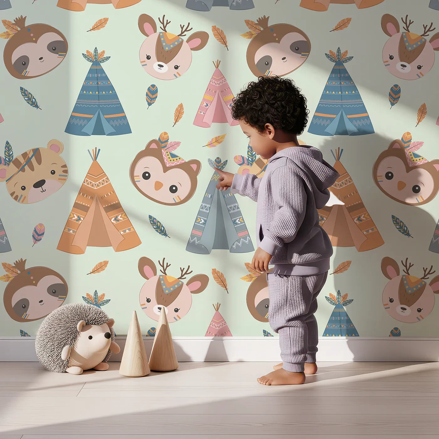 Lovely child standing in front of Whimsy Tots Tribal Pals Wallpaper in Mint Green with owl, sloth, deer, tiger, tent, feather in design.