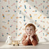Lovely child standing in front of Whimsy Tots Boho Arrows Wallpaper in White with arrow, triangle, dot in design.