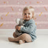 Lovely child standing in front of Whimsy Tots Tribal Sky Dance Wallpaper in Pink with arrow, feather, star, stripe in design.