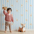 Lovely child standing in front of Whimsy Tots Milky Morning Stripes Wallpaper in Blue with milk, stripe, bottle in design.