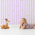 Lovely child standing in front of Whimsy Tots Milky Morning Stripes Wallpaper in Lavender with milk, stripe, bottle in design.