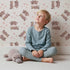 Lovely child standing in front of Whimsy Tots Moo Moo Love Wallpaper in Cream with cow, heart, bell in design.